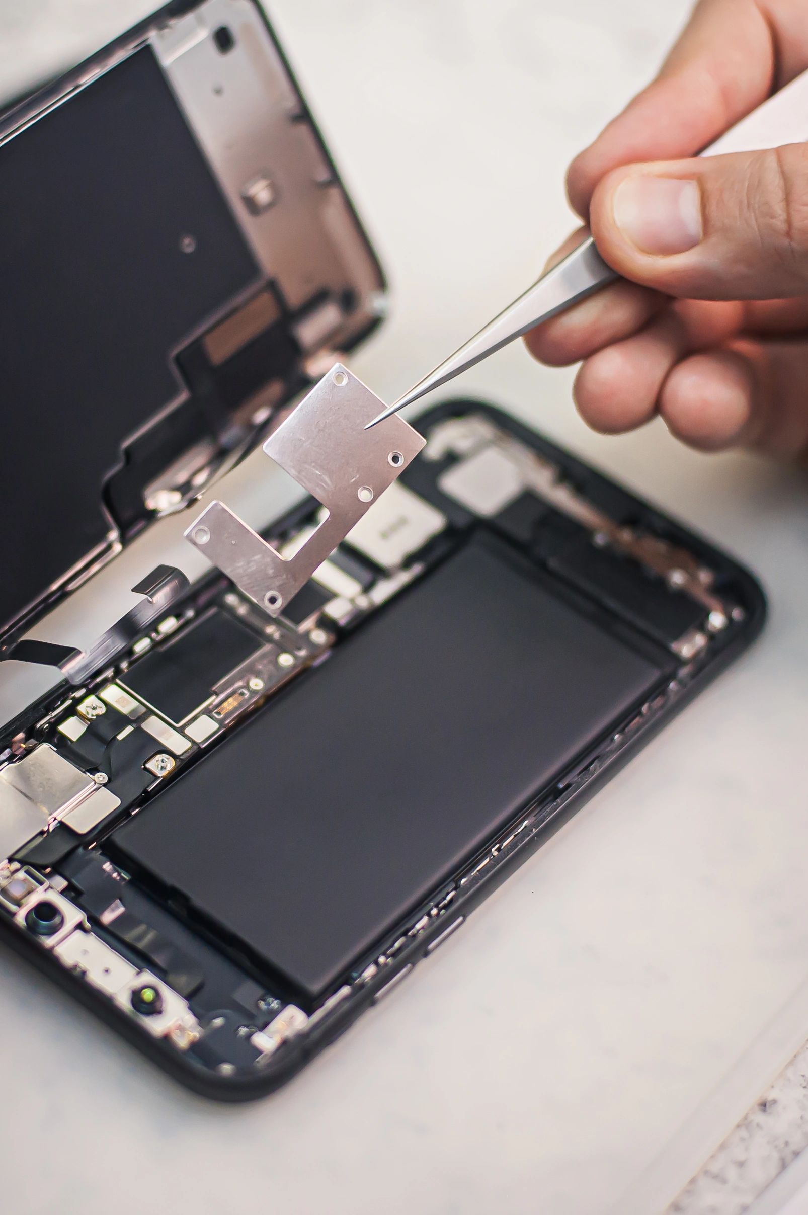 Person repairing a smartphone with tweezers.