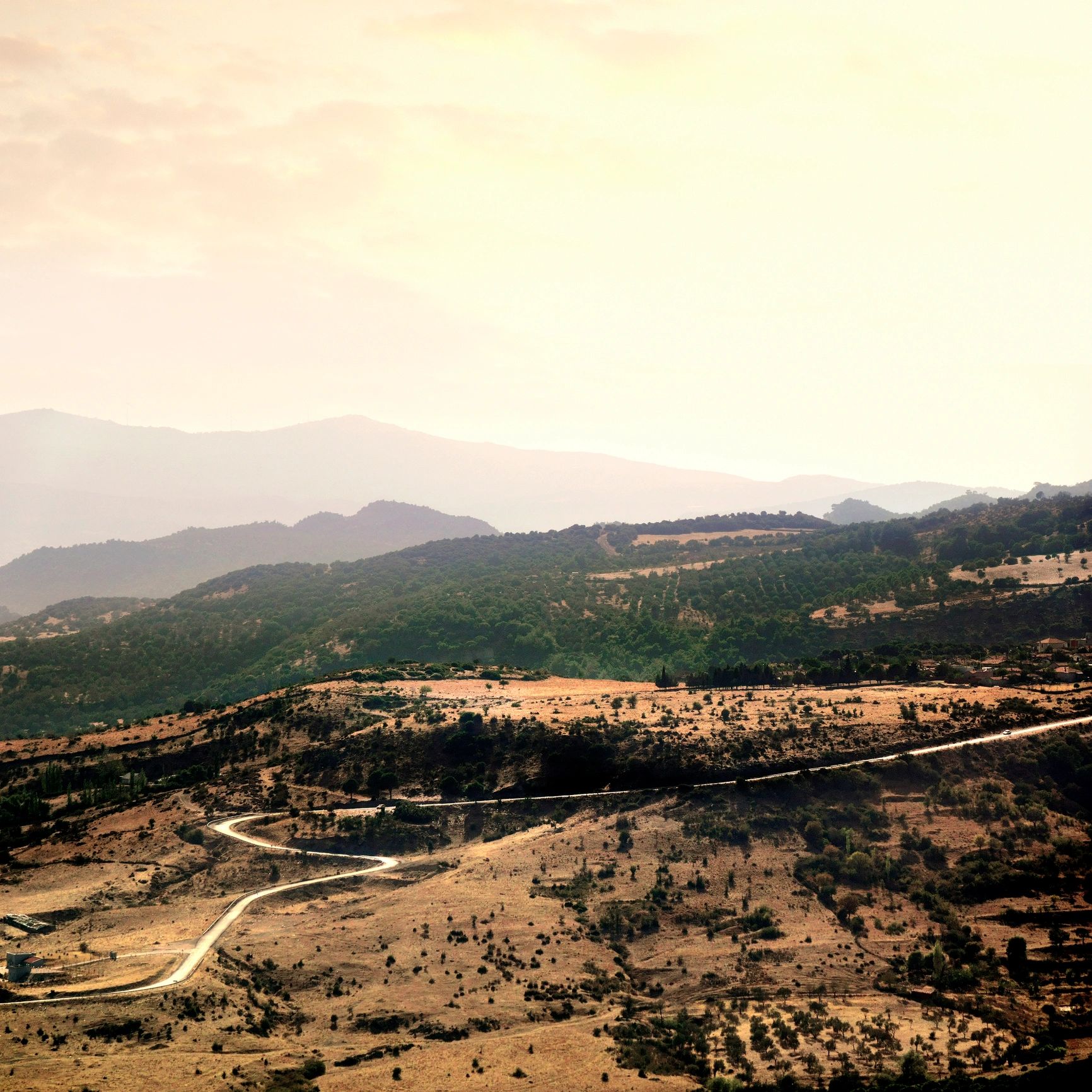Winding road through dry hills with distant mountain layers at sunset.