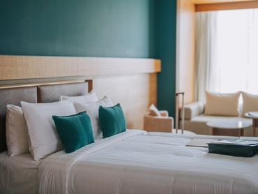 Modern hotel room with neatly made bed and teal accent pillows.