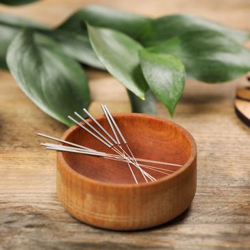 Thin acupuncture needles in a wooden bowl on a natural wooden surface.