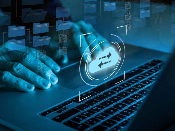 Hands using a laptop with cloud file transfer icons overlay.