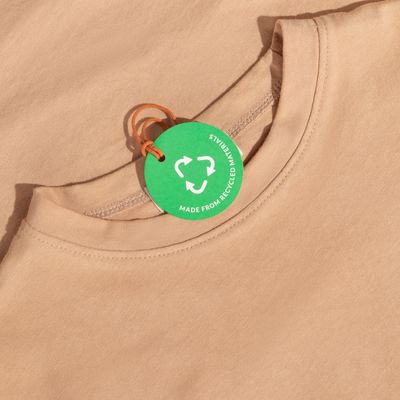 Close-up of a beige shirt with a green recycled materials tag.