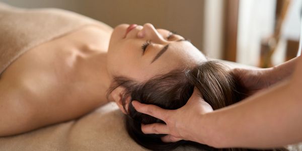 Woman receiving a relaxing head massage while lying on a towel.