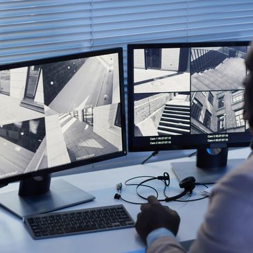 Security officer monitoring multiple surveillance cameras on dual screens.