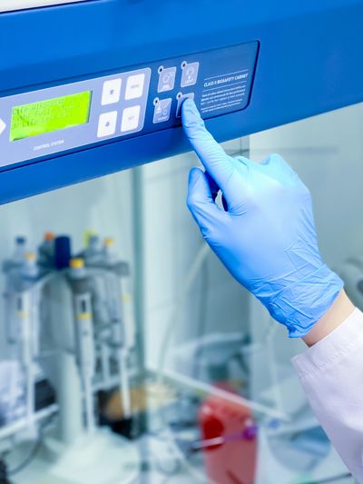 Gloved hand pressing button on lab equipment.