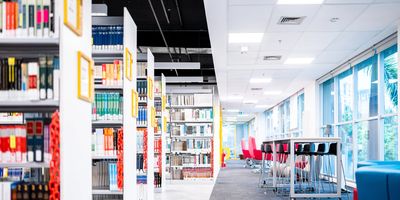 Modern library interior with bookshelves and seating by large windows.