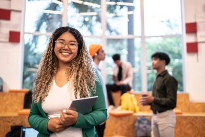 Jeune femme souriante tenant une tablette dans un espace de travail moderne.