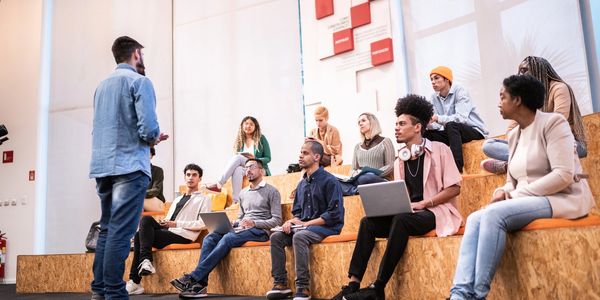 A diverse group attentively listens to a speaker in a modern classroom setting.