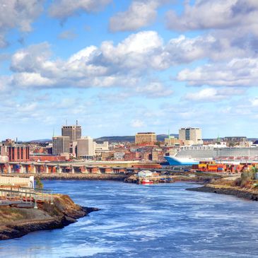 City skyline with river and bridge under a cloudy sky.