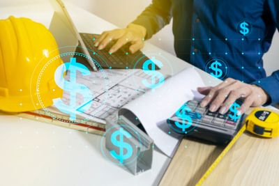 Person calculating construction costs with blue dollar signs overlay.