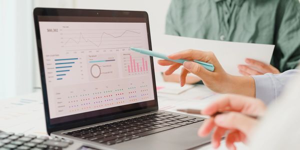 Two people analyzing financial data on a laptop screen with charts and graphs.