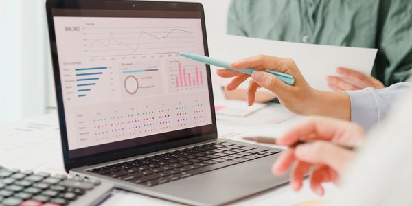 Two people analyzing financial data on a laptop screen with charts and graphs.