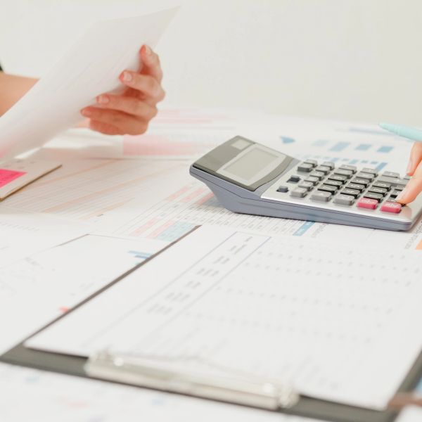 Hands working with calculator and financial documents on a desk.