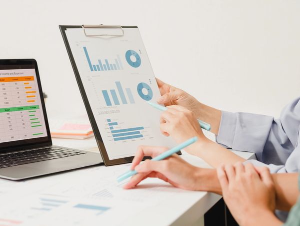 Two people analyzing financial charts and data on paper and laptop.