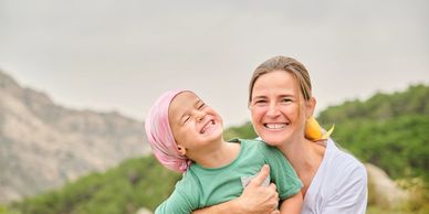 A mom holding her daughter with cancer in nature smiling.