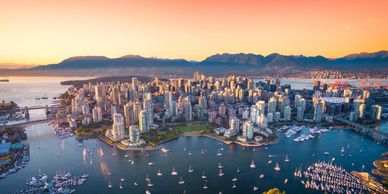Aerial view of a coastal city with boats and mountains at sunset.