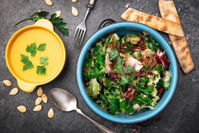 A bowl of fresh green salad with flatbread and a bowl of creamy soup garnished with herbs.