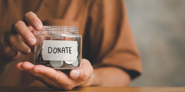 Person holding a jar labeled 'DONATE' filled with coins.