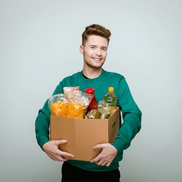 Smiling young man holding a box full of groceries.