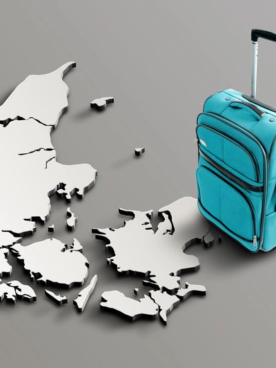 Rolling suitcase placed beside a raised 3D map of Denmark, representing travel preparation and destination planning
