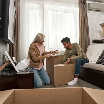 A couple carries boxes, maneuvering around unpacked ones.