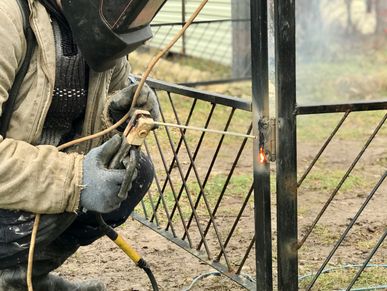 Person welding a metal gate outdoors with protective gloves and mask.