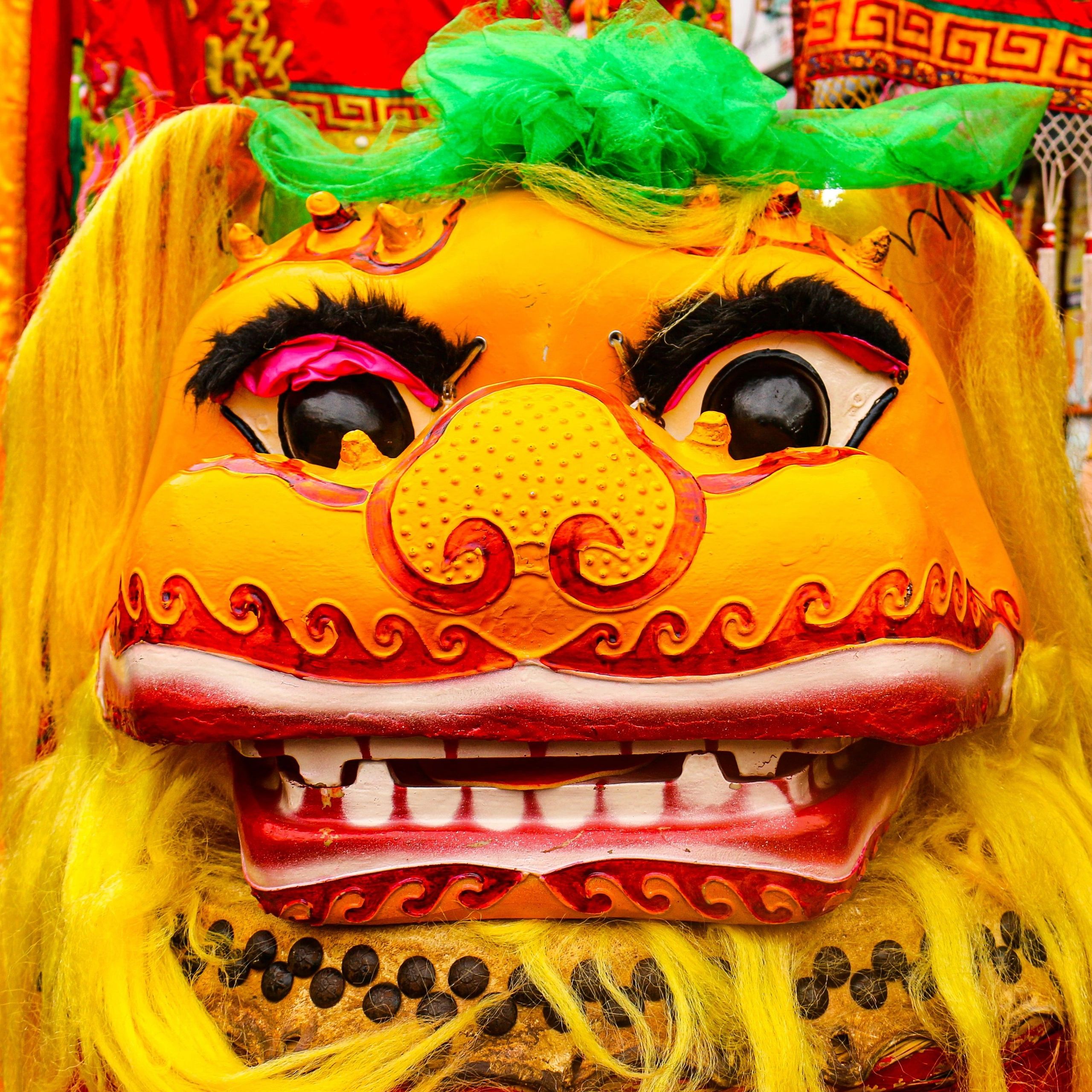Close-up of a vibrant yellow lion dance mask with green and red details.