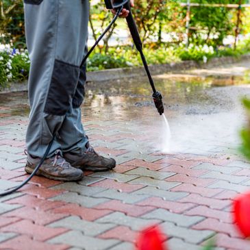 Person pressure washing a brick pavement outdoors.