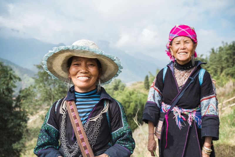 portrait of two smiling indigenous woman from black hmong tribe standing in the sa pa landscape and looking to camera