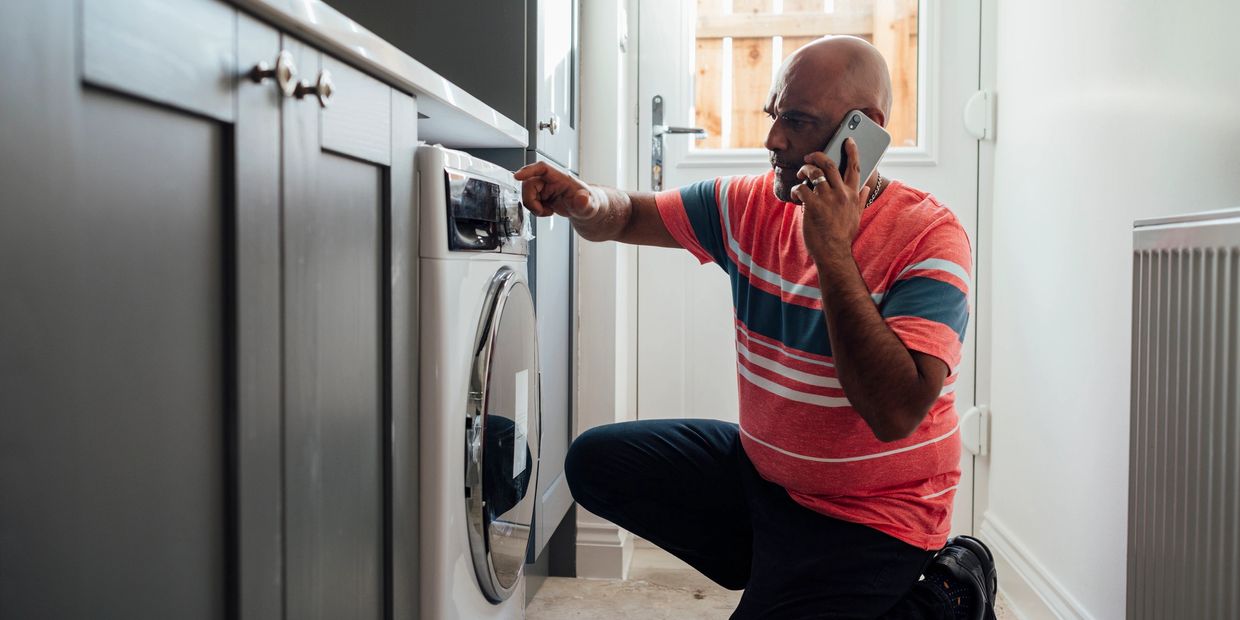 Man kneeling by washing machine, talking on phone and inspecting it.