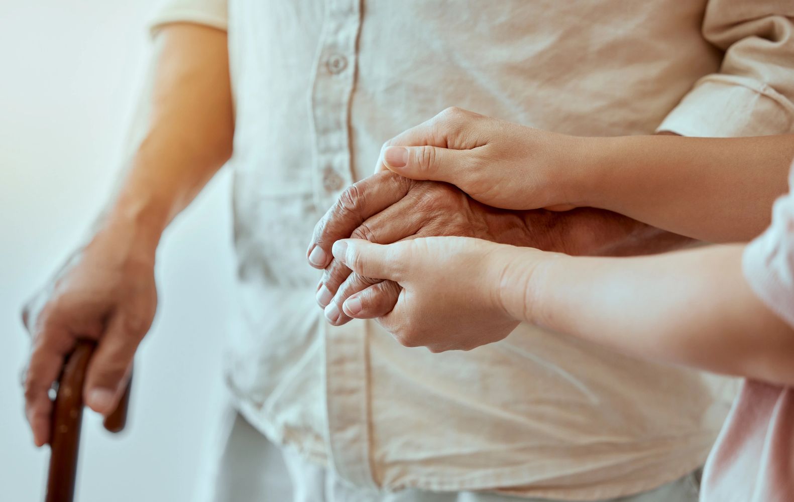 Younger hands gently holding an elderly hand for support and care.