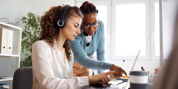 Due donne lavorano insieme con laptop e cuffie.