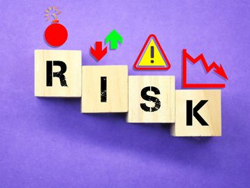 Wooden blocks spell RISK with warning icons on purple background.