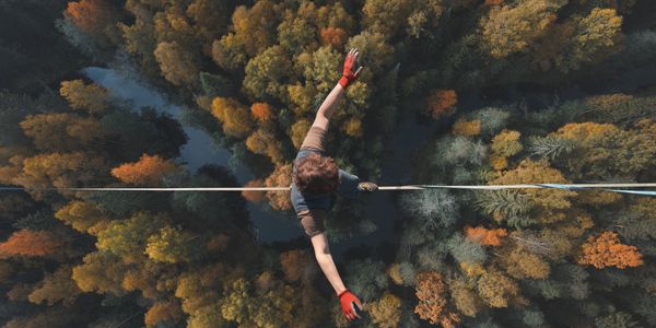 Person walking on a high tightrope above autumn trees.