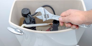 Hand using wrench to fix a toilet tank mechanism.