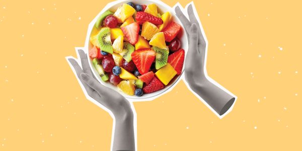 Hands holding a colorful bowl of fresh fruit against a yellow background.