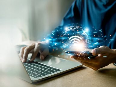 Person using laptop and smartphone with digital Wi-Fi and network icons.