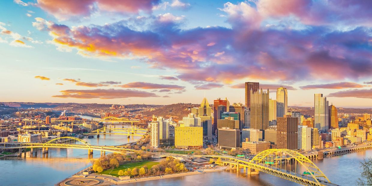 A vibrant city skyline with multiple yellow bridges over a river at sunset.