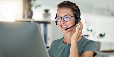 Smiling woman wearing headset working on laptop.
