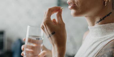 Person holding a pill near their mouth with a glass of water.