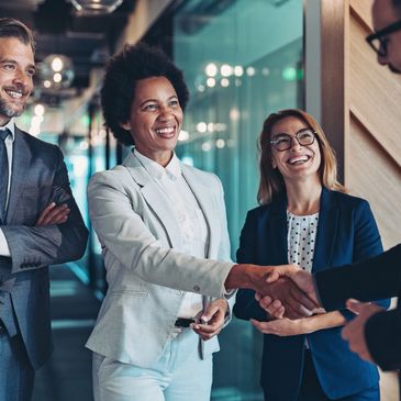Four business professionals smiling and shaking hands in a modern office.
