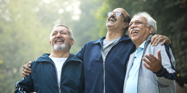 Three elderly men joyfully embracing and laughing outdoors.