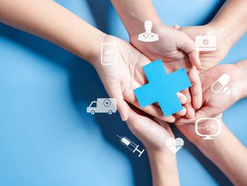 Hands holding a blue medical cross with healthcare icons around them.