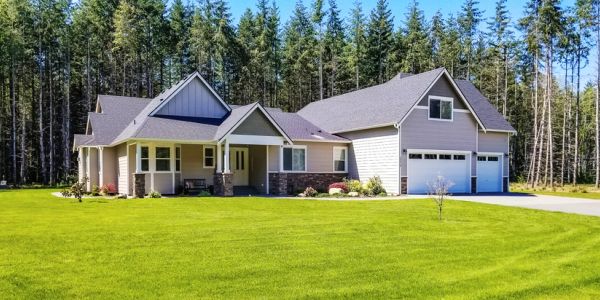 Single-story house with a large lawn and forest backdrop.
