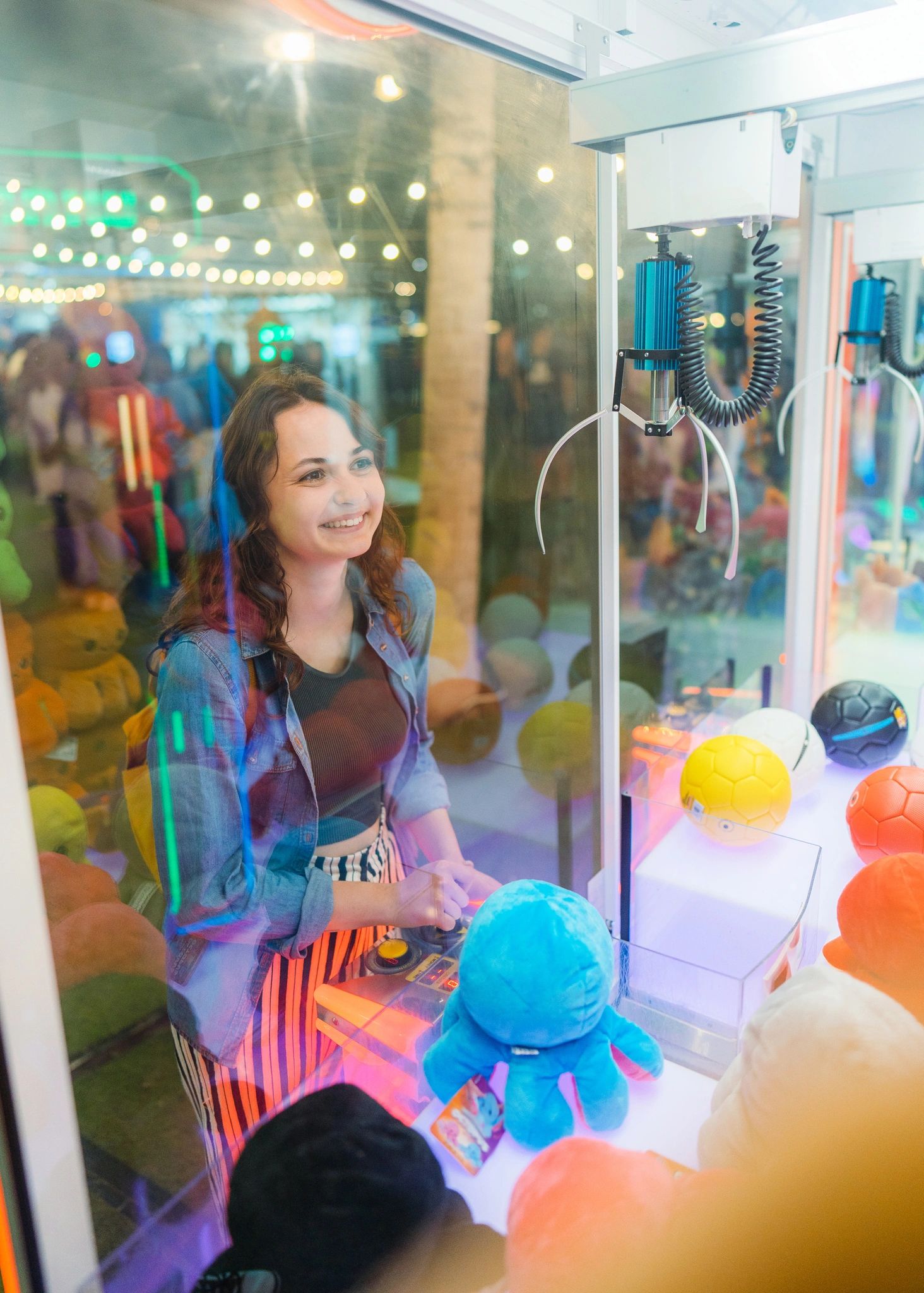 A woman plays a claw machine game, smiling brightly.
