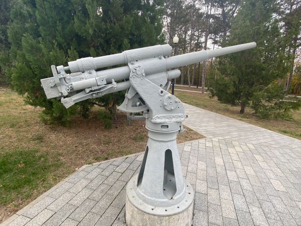 A mounted, gray-painted naval gun displayed outdoors on a paved area.