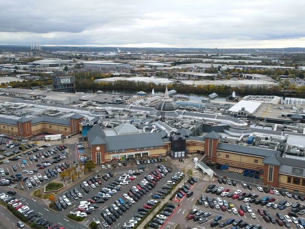 Aerial view of a large shopping center with crowded parking and surrounding industrial area.