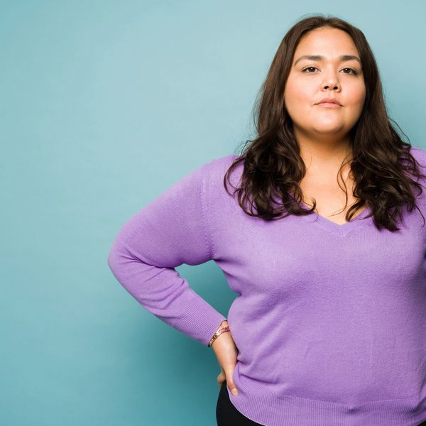Confident woman in purple sweater with hand on hip.