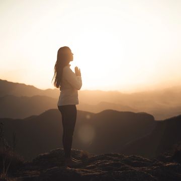 Person praying on mountain during sunset.
