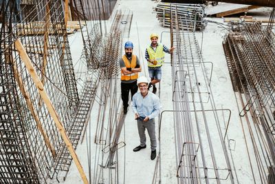 Three construction workers at a building site with steel reinforcements.
